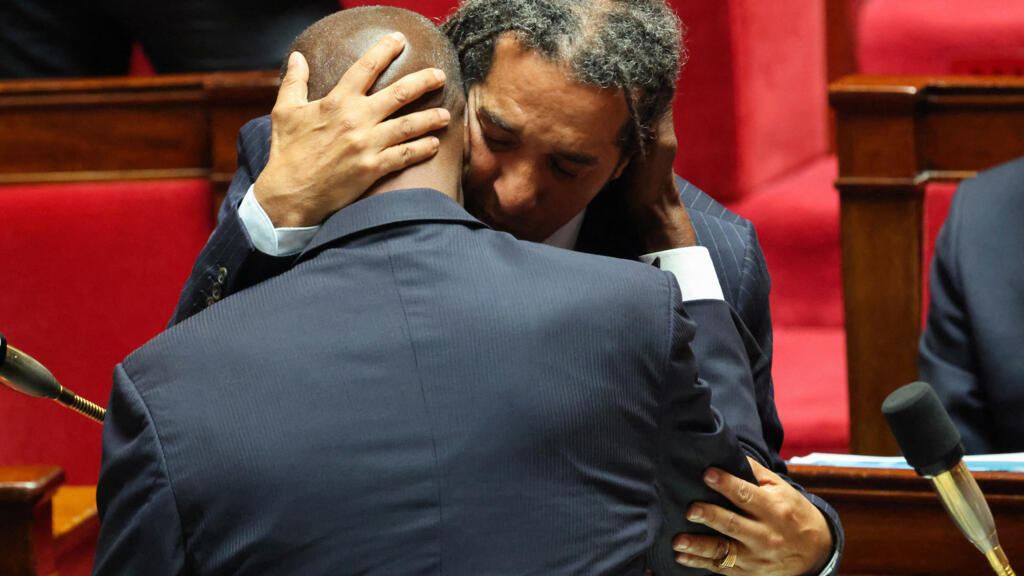 Le député Steevy Gustave (à droite), du groupe Écologiste et social, embrasse le député Max Mathiasin (à gauche), du parti Libertés, Indépendants, Outre-Mer et Territoires, après que sa proposition de loi visant à abolir les lois relatives à l'esclavage a été adoptée à l'unanimité par l'Assemblée nationale, à Paris, le 28 mai 2026.